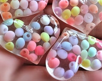 May include: Four clear heart-shaped resin ornaments filled with pastel-colored beads. The beads are in shades of pink, blue, yellow, and green.