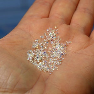 May include: A pile of iridescent clear rhinestones in a hand.