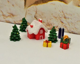 May include: Miniature Christmas village scene featuring a red house with a snow-covered roof, green Christmas trees, and wrapped gift boxes. The scene includes a yellow gift box with a red bow, and two blue rectangular gifts.