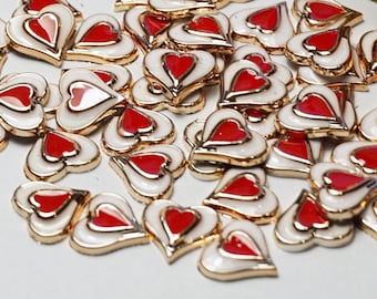 May include: A large pile of red and white heart-shaped charms with gold trim. The charms are scattered on a white surface.