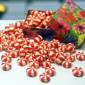 May include: A box of red and white peppermint candies, spilled out on a white surface. The candies are round and have a swirl design.