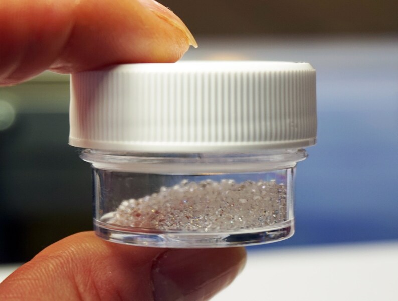 May include: A small clear plastic jar with a white lid filled with clear, shiny crystals.
