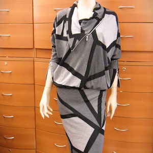 May include: A two-piece outfit on a mannequin. The top is a gray and black geometric pattern with a zipper. The skirt is a matching gray and black geometric pattern. The mannequin is standing in front of a wooden cabinet.