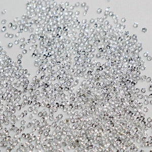 May include: A large quantity of small, clear, faceted rhinestones scattered on a white surface.