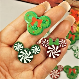 May include: Assortment of green and red glitter Christmas ornaments shaped like Mickey Mouse ears. The ornaments feature a candy cane design and a wreath design.