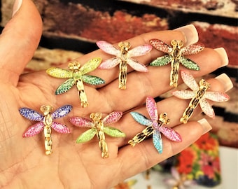 May include: Assortment of colorful dragonfly-shaped embellishments with gold accents. Each dragonfly has a different color and glitter finish.
