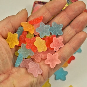 May include: A hand holding a variety of star-shaped gummy candies in assorted colors, including pink, blue, yellow, orange, and green.