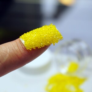 A close-up of a finger with a yellow nail polish with small yellow beads on top.