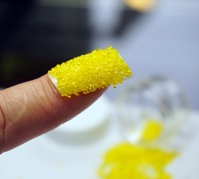 A close-up of a finger with a yellow nail polish with small yellow beads on top.