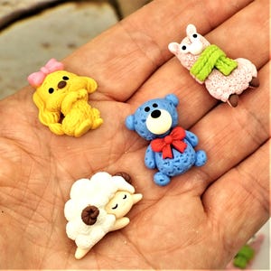 May include: A collection of miniature animal figurines. Includes a yellow dog with a pink bow, a blue teddy bear with a red bow, a pink llama with a green scarf, and a white sheep with brown accents.