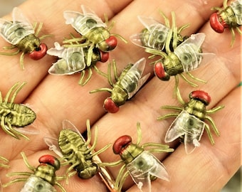 May include: A collection of small, detailed insect figurines. The insects have a green body, transparent wings, and a red head. The figurines are arranged on a light-colored surface, showcasing their intricate design and realistic appearance.