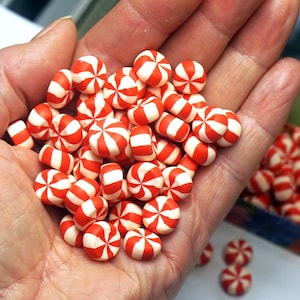May include: A collection of small, round, peppermint-style candies featuring a vibrant red and white spiral pattern. These circular sweets are uniform in size and shape, displaying a distinct pinwheel design across their smooth, glossy surfaces.