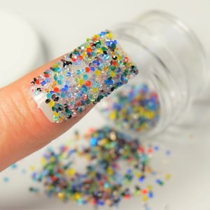 May include: A fingernail with a thick layer of colorful rhinestones, with a jar of loose rhinestones in the background.