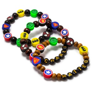 May include: Three colorful beaded bracelets with superhero logos and names "Charlie" and "Matteo" spelled out in black beads.
