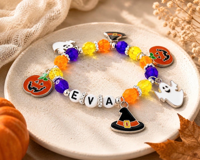 May include: A beaded bracelet featuring alternating yellow, orange, and purple faceted beads, silver-toned spacers, and white letter beads spelling EVA. The bracelet includes metal charms shaped like pumpkins, ghosts, and a black witch hat.