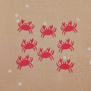 May include: Eight red paper cutouts of crabs on a beige background with white polka dots.