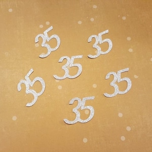 May include: Six silver glitter number 35s on a brown background.