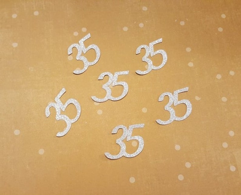 May include: Six silver glitter number 35s on a brown background.