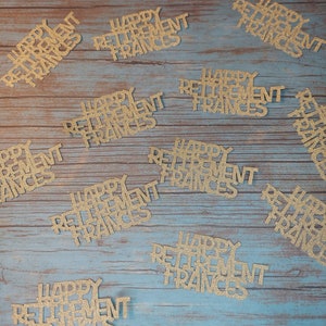 K&ouml;nnte beinhalten: Goldene Konfetti mit Glitzer und dem Text "Happy Retirement Frances" auf einer blauen Holzoberfl&auml;che verstreut.