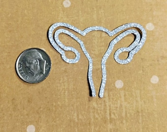 May include: A silver glitter cutout of a female reproductive system, approximately the size of a US dime.