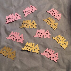 May include: Pink and gold glitter confetti with the name "Mila Jayde" written on each piece.