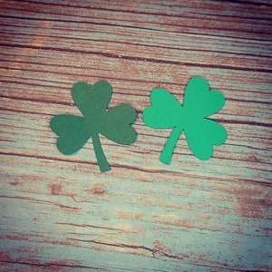 May include: Two green paper shamrocks on a rustic wooden background.