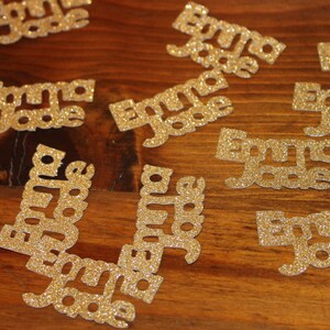 May include: A collection of gold glitter paper cutouts with the name "Emma Jade" written on each one.