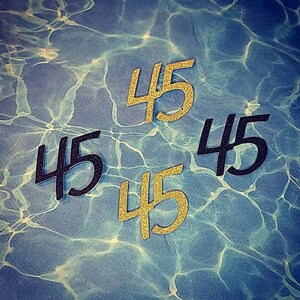 May include: Four black and gold paper cutouts of the number 45. The cutouts are arranged in a diamond shape on a blue and white background.
