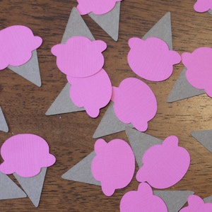 May include: Pink and gray paper ice cream cone cutouts. The ice cream cones are scattered on a wooden surface.
