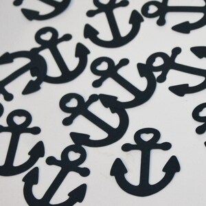 May include: A collection of navy blue anchor cutouts scattered on a white surface. Each anchor features a heart-shaped detail at the top. The nautical-themed cutouts are ideal for crafting or decorative projects.