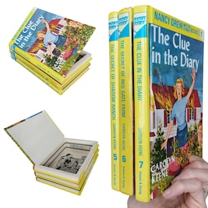 May include: A collection of vintage Nancy Drew mystery books. The books have yellow spines and covers with colorful illustrations. The titles include "The Clue in the Diary" and "The Secret of Shadow Ranch." One book is open, revealing a hidden compartment.