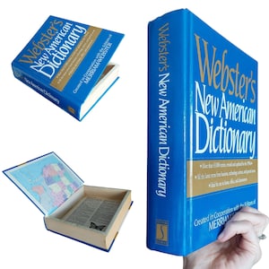 May include: A hollowed-out blue Webster's New American Dictionary book safe with gold lettering on the cover. The interior features a map on the inside cover and a butterfly illustration on the bottom of the compartment, revealing a hidden storage space.