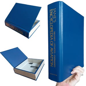 May include: A blue hardcover book titled "Jane's Encyclopedia of Aviation" with gold lettering. The book is shown closed and open, revealing a hidden compartment. The book is held by a person.