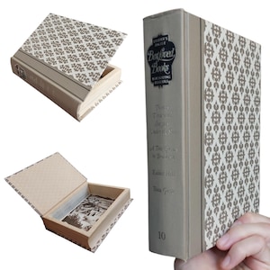 May include: A hollowed-out book box with a beige spine and a brown and white damask pattern on the cover. The spine features the text Reader's Digest Best Loved Books For Young Readers, Twenty Thousand Leagues Under the Sea, A Tree Grows in Brooklyn, Rabbit Hill, Beau Geste, and the number 10. The interior is lined with a black and white illustration.