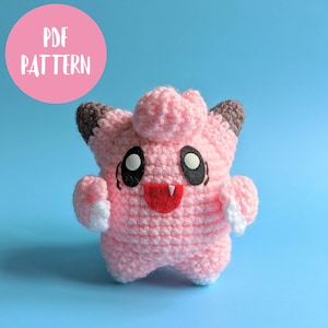 Könnte beinhalten: Ein handgefertigtes rosa Häkeltier mit schwarzen Augen, einer roten Zunge und weißen Akzenten. Das Spielzeug hat graue Ohren und steht auf blauem Hintergrund. Ein rosa Kreis mit den Worten "PDF PATTERN" befindet sich in der oberen linken Ecke.