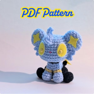 Puede incluir: Un juguete de peluche azul tejido a ganchillo con detalles de estrellas amarillas en las orejas y ojos ovalados amarillos. El juguete tiene patas negras y un torso a rayas amarillas y negras. El texto "PDF Pattern" está encima del juguete.