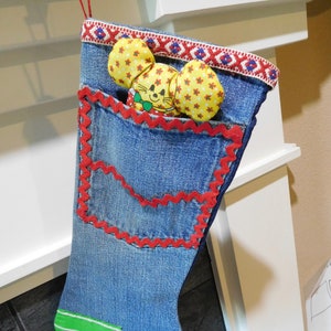 以下が含まれることがあります： 赤と白の縁取り、緑と白のストライプの生地のパッチ、赤とオレンジの生地のパッチが付いた青いデニムのクリスマスストッキング。ストッキングの中には黄色と赤のネズミの玩具が入っています。