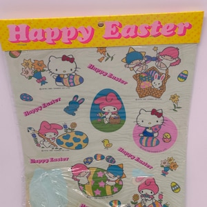 May include: A sheet of Easter stickers featuring Sanrio characters like Hello Kitty. The stickers depict decorated eggs, bunnies, and the text "Happy Easter" in pink on a yellow banner. The stickers are packaged in clear plastic.