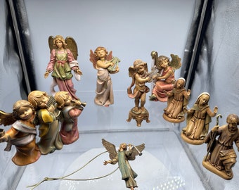Puede incluir: Una colección de nueve figuritas pintadas a mano que representan ángeles y figuras bíblicas. Las figuritas están hechas de un material marrón claro y presentan detalles intrincados. Los ángeles están tocando instrumentos musicales, mientras que las figuras bíblicas visten túnicas tradicionales.