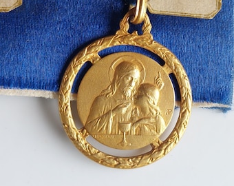 May include: Gold-toned metal pendant featuring a religious image of Jesus Christ and a child holding a chalice. The pendant is surrounded by a decorative wreath design.