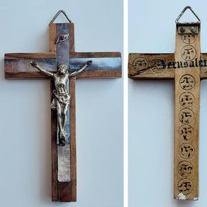 May include: Wooden cross with a silver Jesus figure. The cross has a dark wood frame with inlaid mother-of-pearl and a metal hanging loop. The back of the cross has the word "Jerusalem" and other symbols.