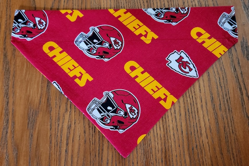 May include: Red and yellow dog bandana with a repeated pattern of a football helmet and the word "Chiefs".