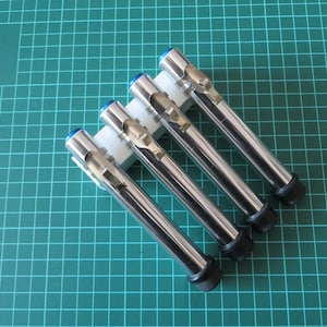 May include: Four silver spark plug testers with blue and black accents are displayed in a white plastic holder.