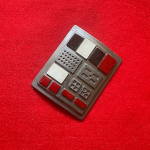 May include: A gray metal panel with a variety of buttons and switches. The buttons are red, black, and white. The panel has a textured surface.