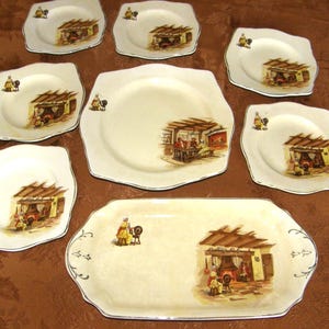 May include: Set of nine vintage ceramic plates featuring a cottage scene design. The plates are white with brown and yellow accents. The plates come in various sizes and shapes, including round, square, and rectangular.