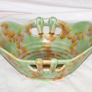 May include: A green ceramic bowl with a floral pattern in shades of brown and purple. The bowl has cut-out handles on the sides.
