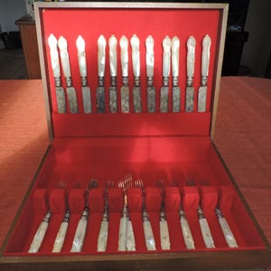 May include: A wooden box with a red velvet interior, containing a set of 24 silver knives and forks with mother-of-pearl handles.