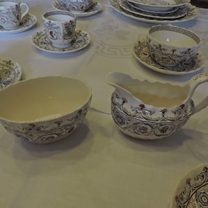 May include: A set of vintage floral patterned teacups, saucers, and a creamer. The cups and saucers are white with a blue, red, and brown floral pattern. The creamer is white with a blue, red, and brown floral pattern.