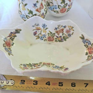 May include: A white porcelain serving dish with a scalloped edge and floral pattern. The dish features a delicate floral design with butterflies and a light pink, blue, and yellow colour scheme.