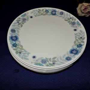 May include: A set of four white ceramic dinner plates with a blue and green floral pattern around the rim.